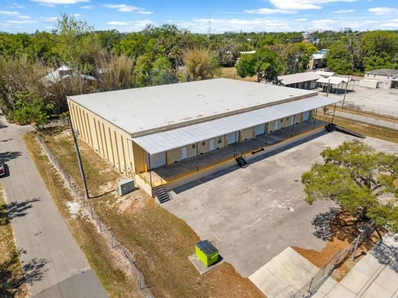 Aerial view of the covered loading dock at 1030 SE 4th Street, Gainesville, FL, with multiple roll-up doors, dock stairs and ramp, and the fenced concrete yard