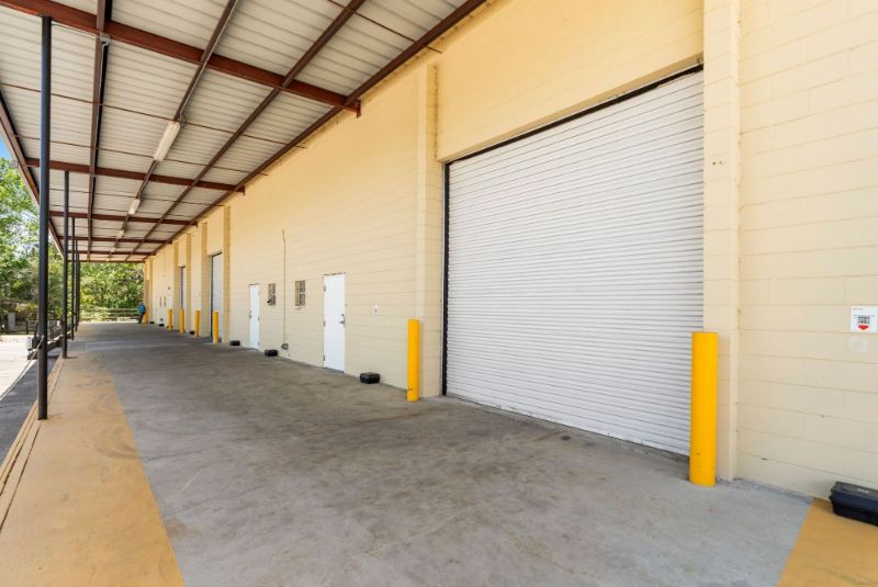 View down the length of the covered loading dock at 1030 SE 4th Street with roll-up doors, man doors, safety bollards, and overhead lighting